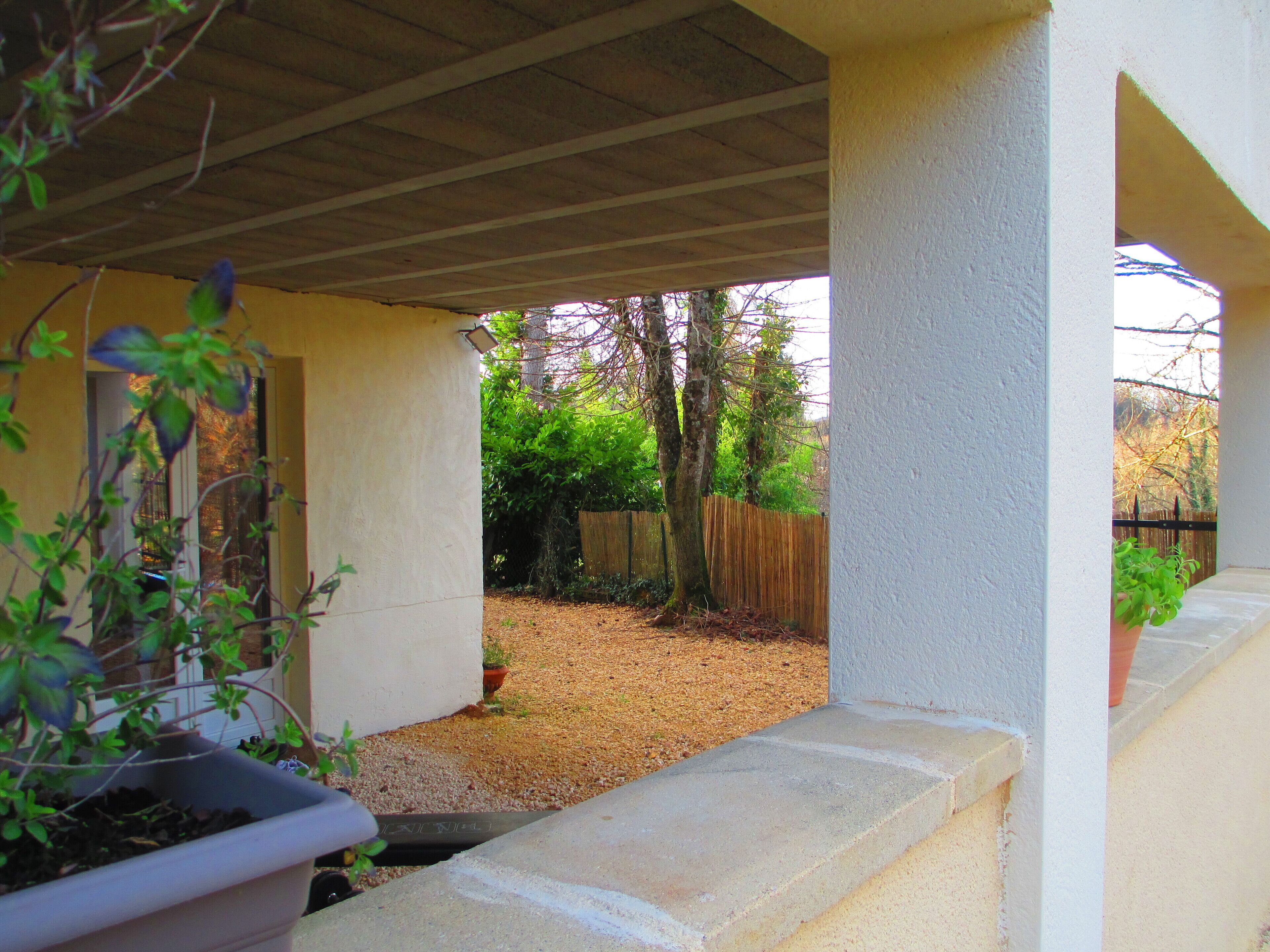 Ein überdachter Patio-Bereich mit Betonboden, Holzlattenzaun und einer Topfpflanze.
