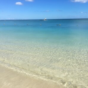A clear beach with calm waters, a distant boat, and a few buoys.