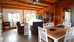 A wooden cabin interior with a dining table, white chairs, a ceiling fan, and a fireplace.
