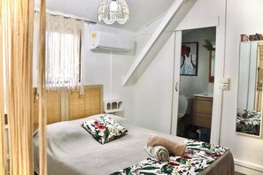 A bedroom with a bed, a window with curtains, a wall-mounted air conditioner, a mirror, and a staircase. - STUDIO PASSION, 300m from the beach (Saint-Paul)