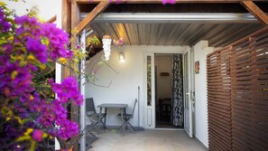 A covered outdoor area with a table and chairs, a wooden fence, and a door leading inside. - STUDIO PASSION, 300m from the beach (Saint-Paul)