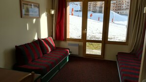 A room with a sofa, a chair, a window with a view of a snowy outdoor area, and a framed picture on the wall.
