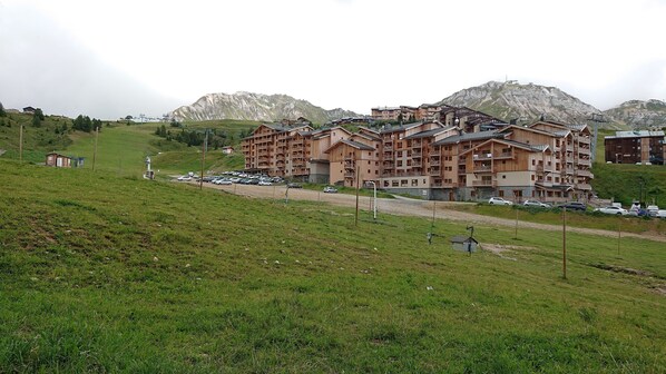 A multi-story wooden building with balconies, surrounded by a parking lot and a grassy hill.