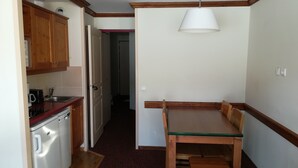 A compact kitchen with wooden cabinets, a refrigerator, a sink, and a dining table with chairs.