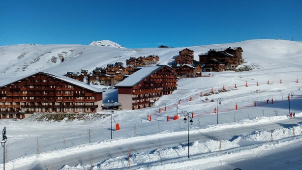 A snow-covered mountain resort with wooden buildings, ski slopes, and orange safety cones.