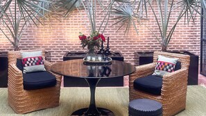 A wicker sofa set with cushions, a round table, and a vase with flowers.