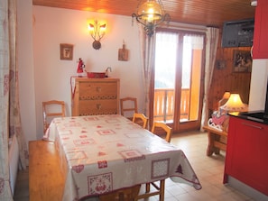 A cozy dining area with a table set for two, a wooden cabinet with drawers, a chandelier, and a television mounted on the wall.