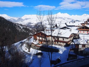 Ein verschneites Bergdorf mit traditionellen Holzhäusern, einer Serpentinenstraße und blauem, klarem Himmel.