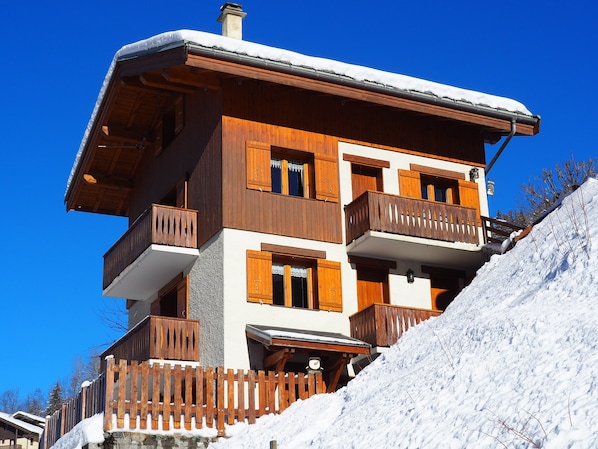 A multi-story wooden building with balconies, a wooden fence, and a snowy slope.