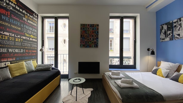 Et moderne hotelværelse med en sort sofa, en seng, et lille rundt bord og en væg med farverig kunst.
