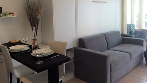 A modern living room with a grey sofa, a dining table with plates and glasses, and a vase with branches. - Melo's Studio with amazing views of Cannes and the sea as well as WiFi (Cannes)