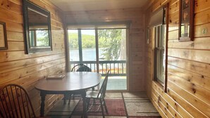 A wooden cabin with a round table and chairs, a window with a view of a lake, and a door leading outside. - 2 BR Waterfront Lodge Suites Overlooking the Docks and Mountains Sunsets! (Lake Luzerne)