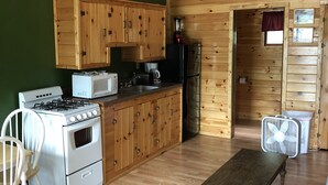 Een kleine keuken met houten kastjes, een fornuis, en een eethoek met een tafel en stoelen.