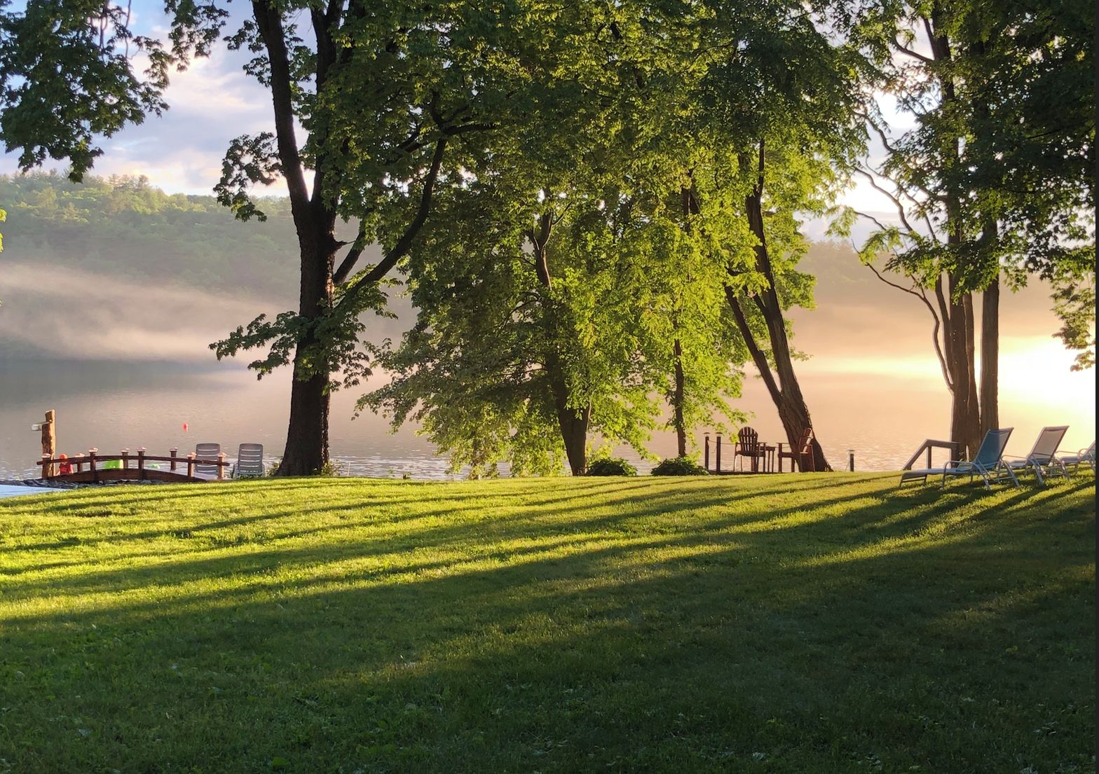 Un parc paisible au bord du lac, doté d’une terrasse en bois et de chaises longues.