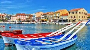 A waterfront scene with boats docked, a row of colorful buildings, and a clear blue sky.