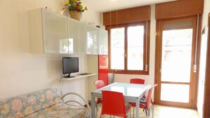 Um espaço compacto com sofá, mesa de jantar com cadeiras, TV em uma prateleira e janela com vista.
