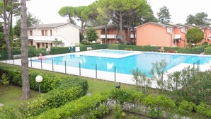 Uma piscina retangular cercada por uma grade, com edifícios altos próximos e vegetação exuberante.