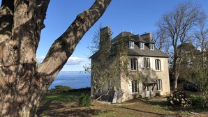 Una casa de dos pisos con fachada de piedra, grandes ventanales y vista al mar.