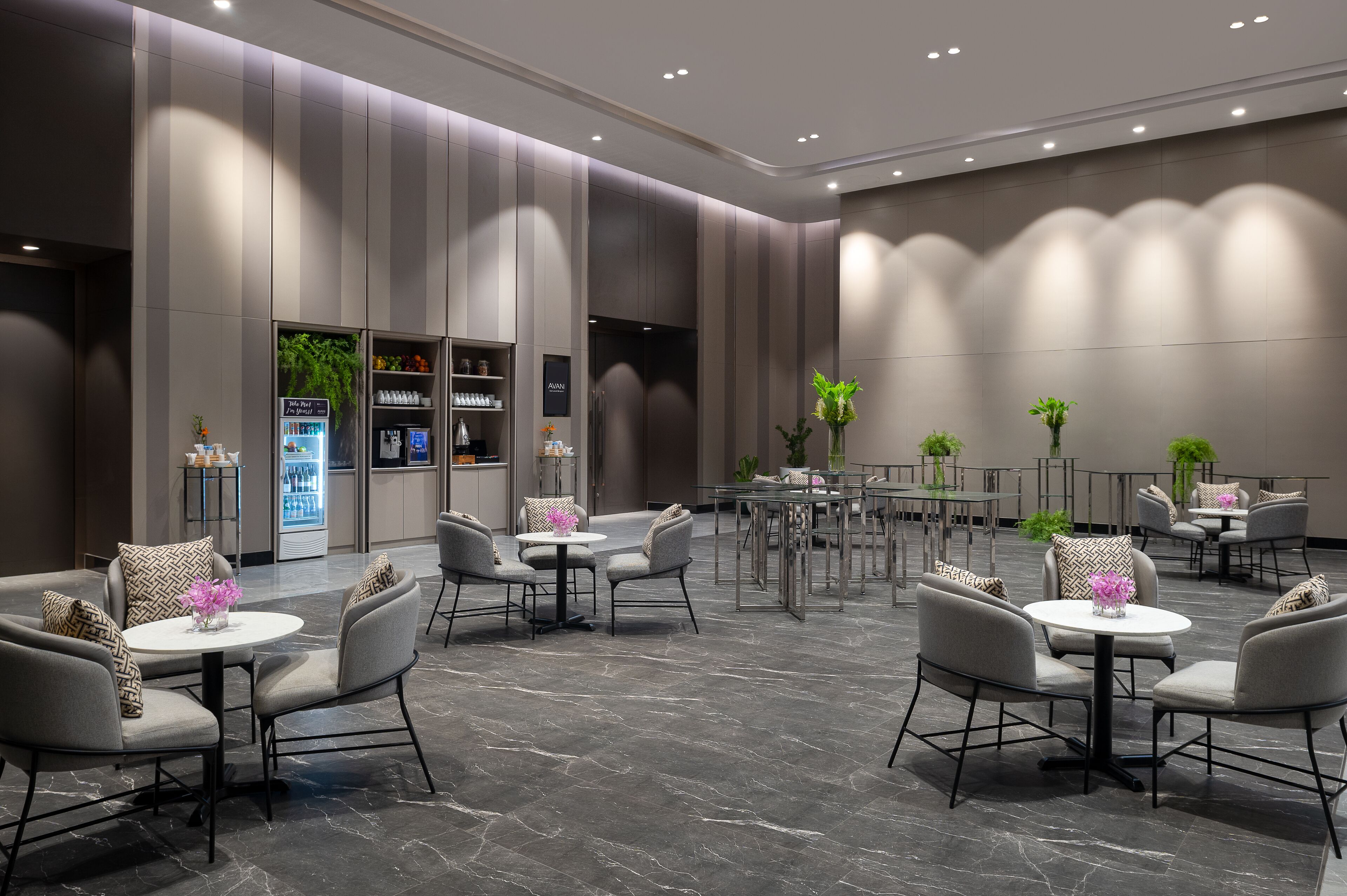 A modern hotel lobby with a central seating area, a minibar, and a reception desk.