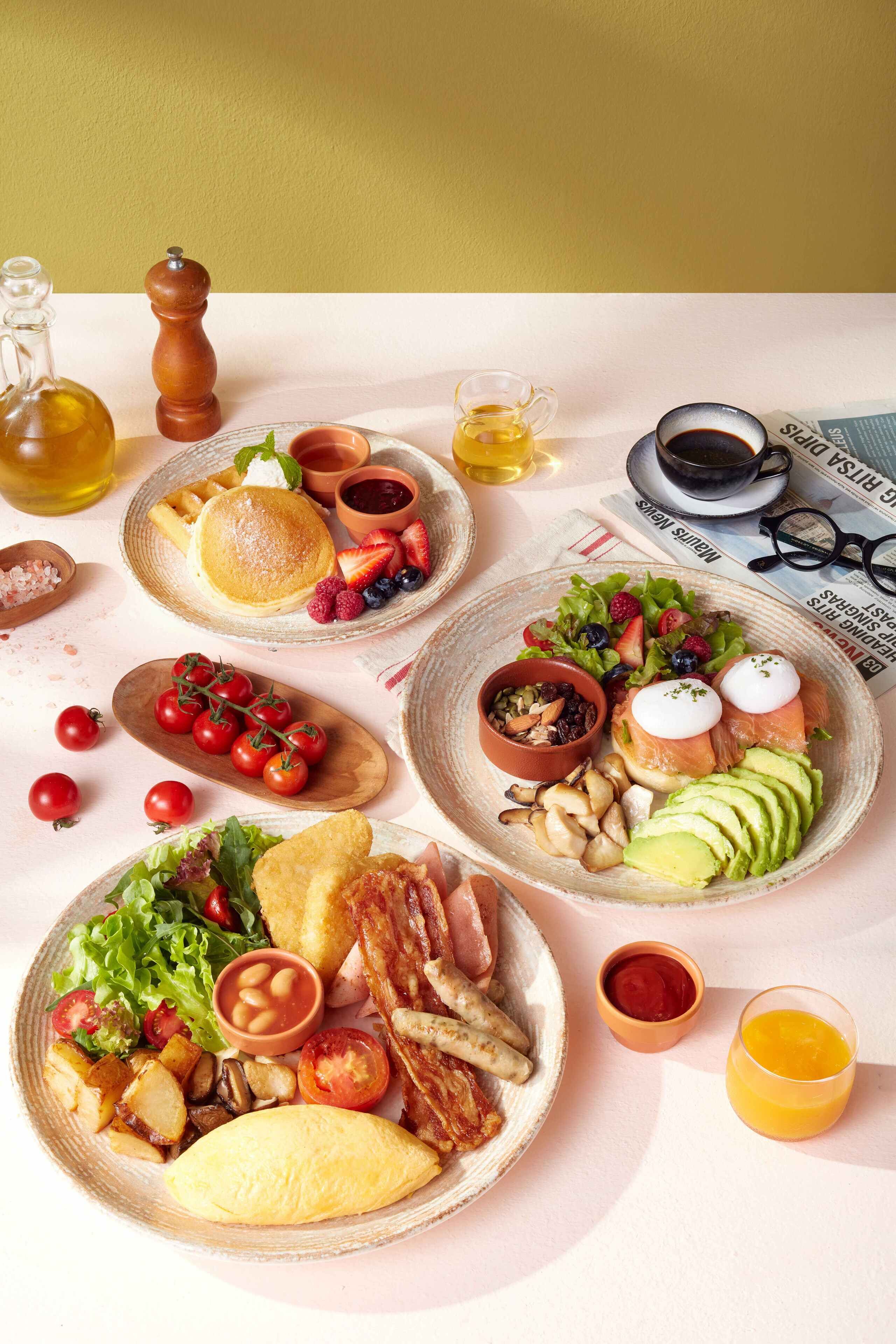 Ein Frühstückstisch mit verschiedenen Speisen, darunter Pfannkuchen, Eier, Speck und Toast, sowie Getränke und Beilagen.