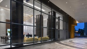 Een moderne hotellobby met een glazen gevel, een receptiebalie en een zithoek met gele banken.