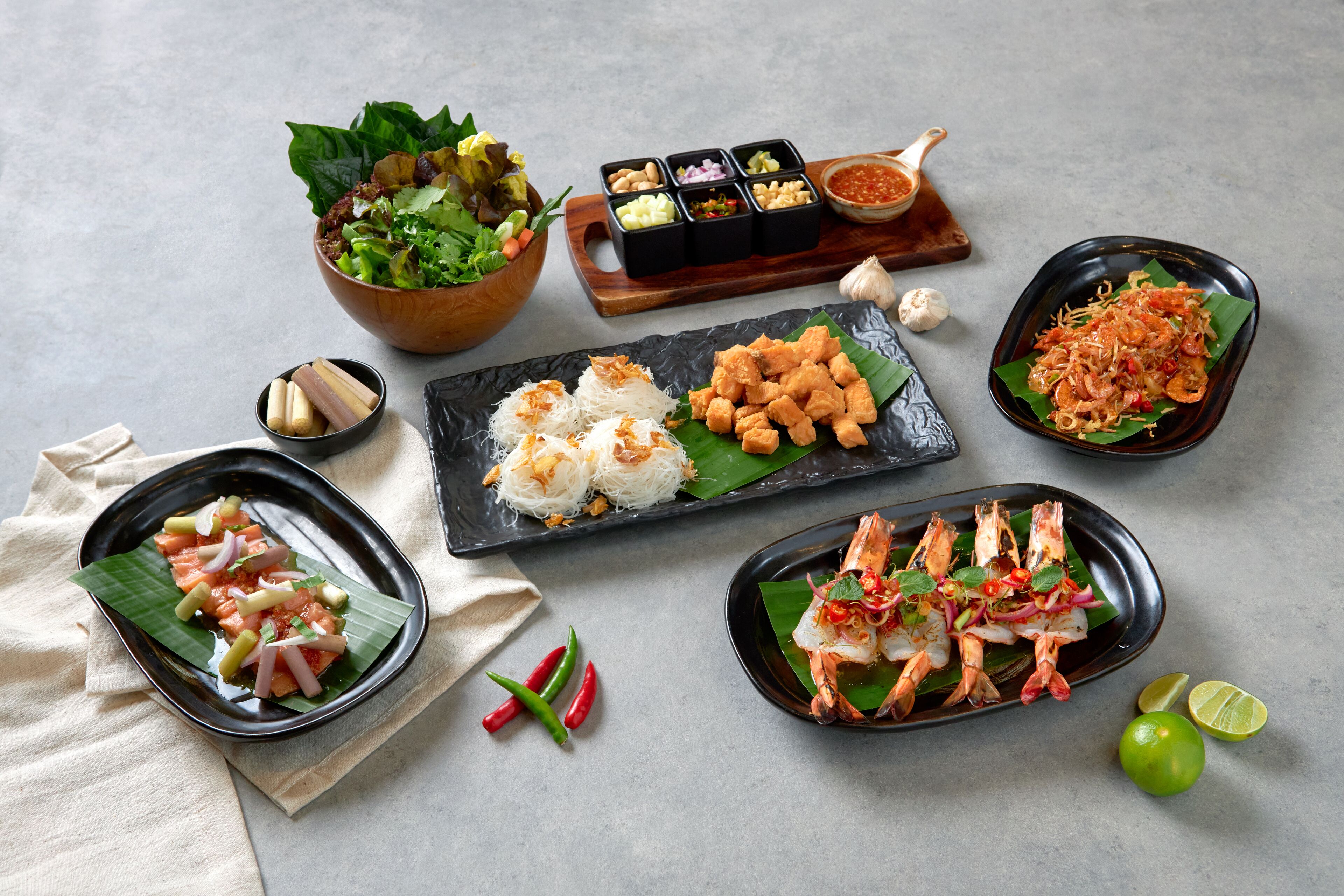 Une variété de plats, notamment des crevettes, du riz et une salade, disposés sur une table sur fond neutre.