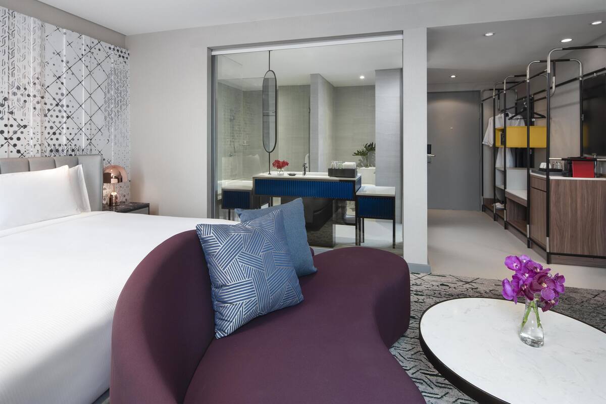 Une chambre d’hôtel moderne dotée d’un grand lit, d’un canapé, d’une table ronde avec un vase, d’une salle de bain avec un miroir et d’une kitchenette.