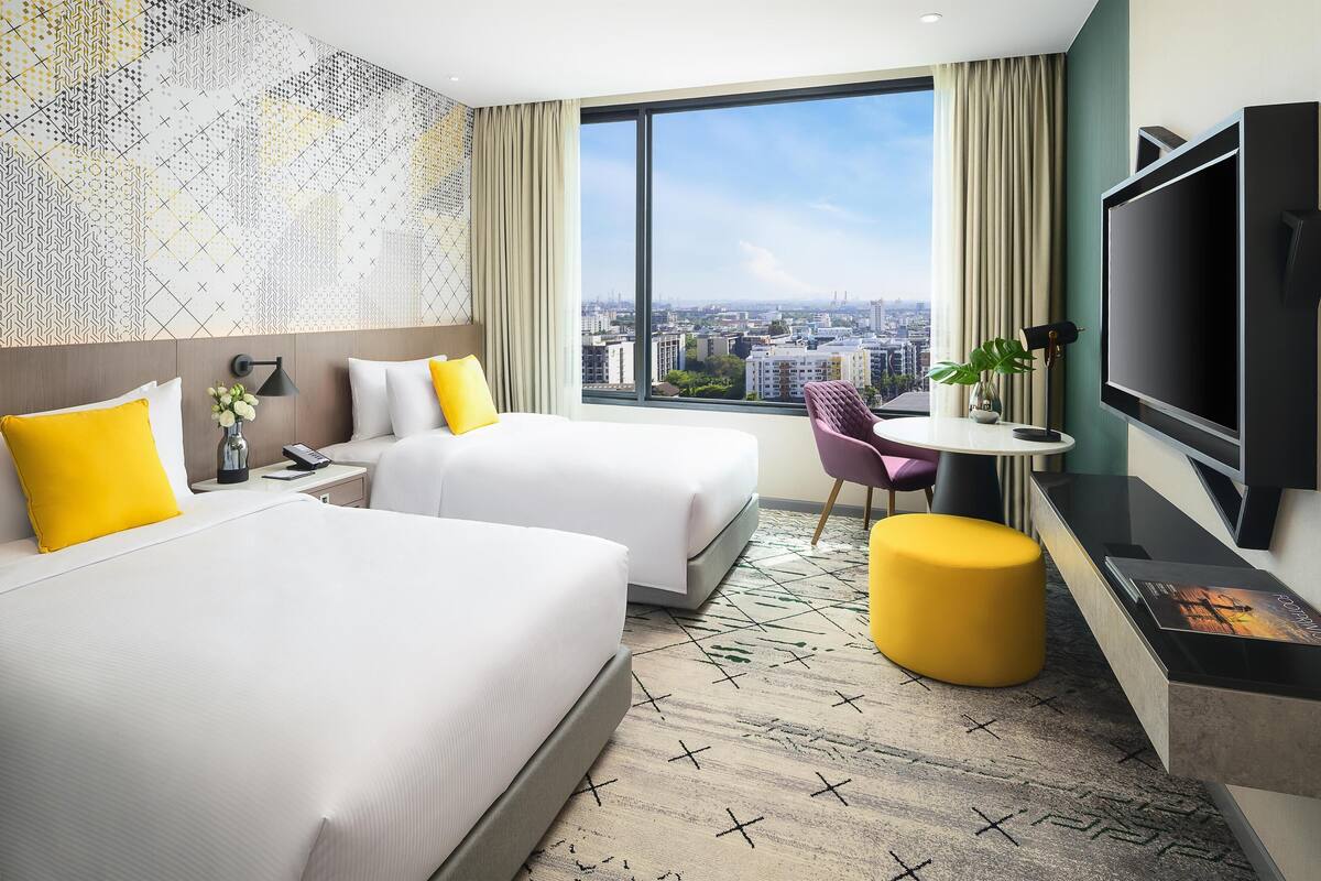 Une chambre d’hôtel avec deux lits, une télévision, un bureau et une grande fenêtre donnant sur la ville.