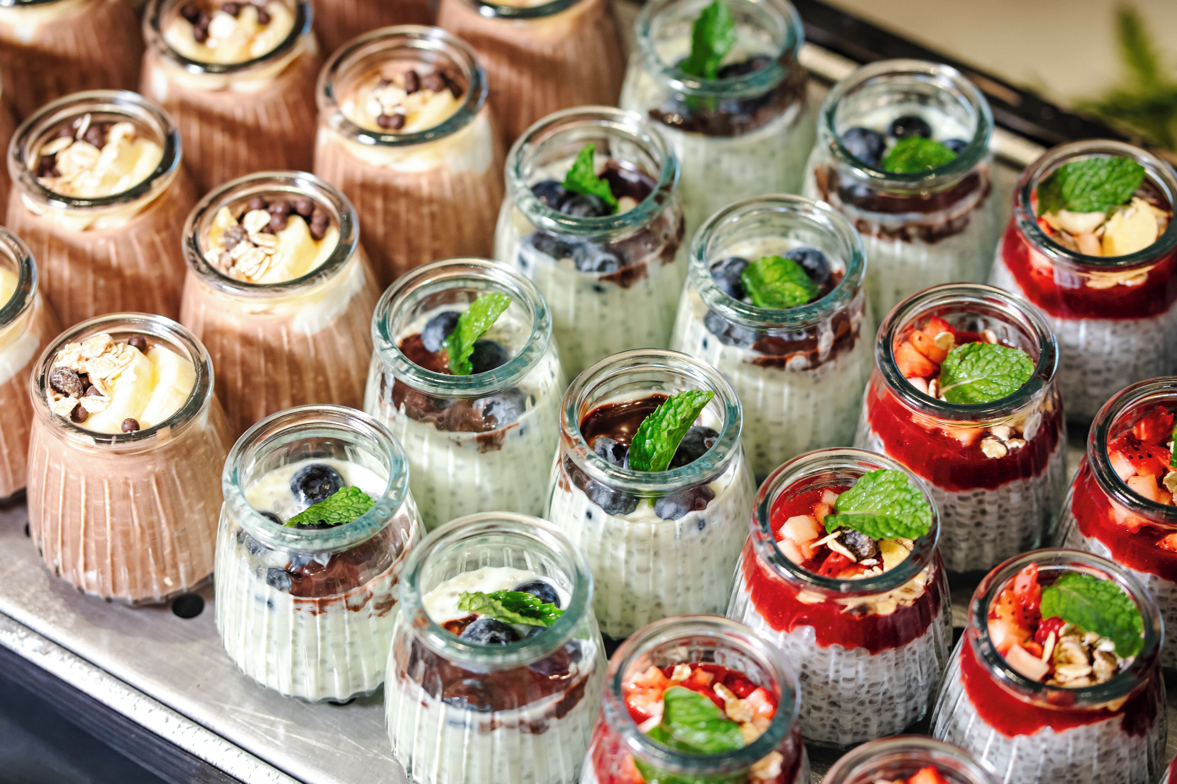 A variety of dessert parfaits in glass jars, each topped with different ingredients like fruits, nuts, and mint leaves.