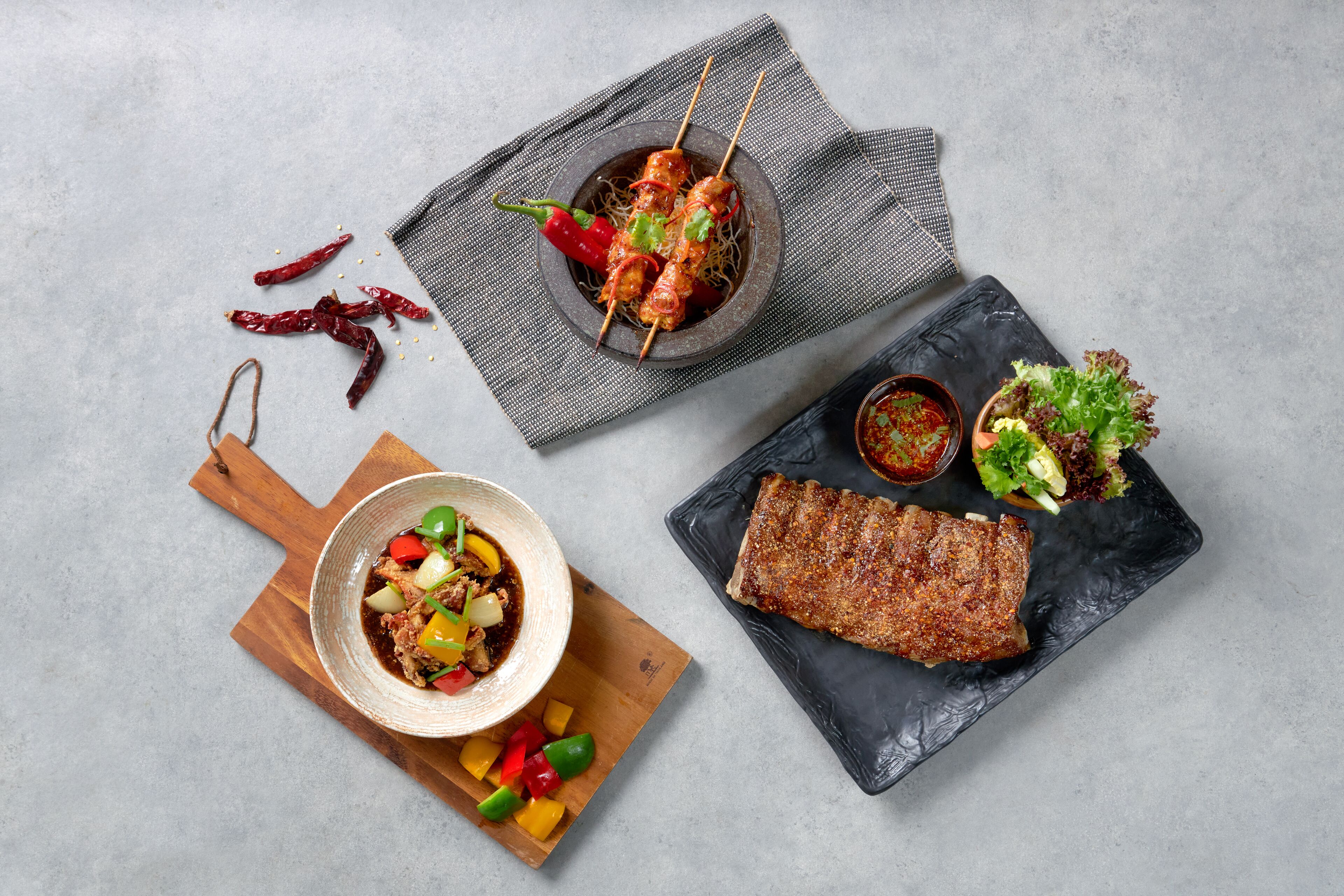 Una comida con brochetas, un tazón de sopa y un bistec a la parrilla sobre una tabla de pizarra.