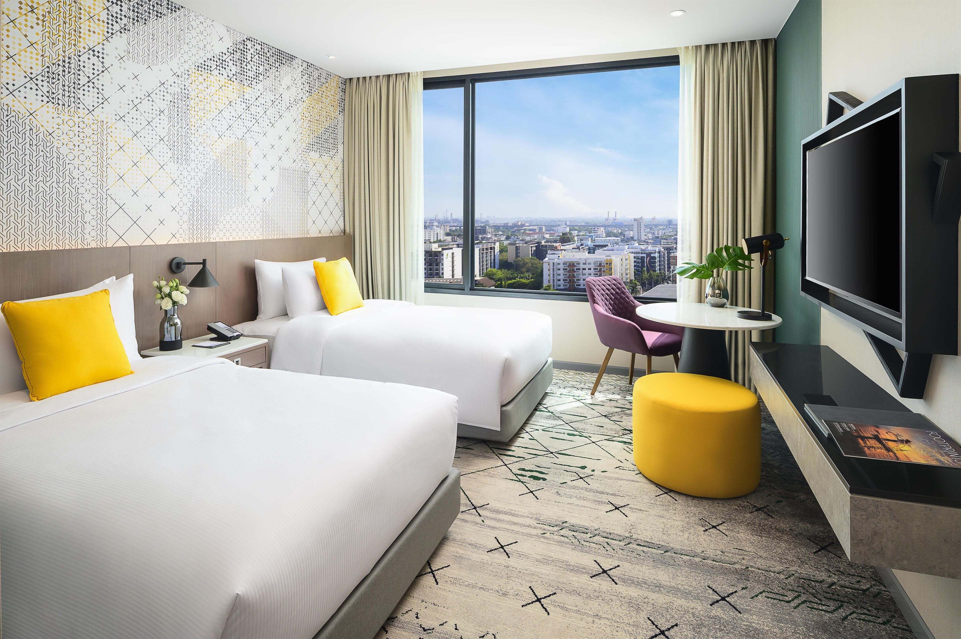 Habitación de hotel con dos camas, un escritorio, una silla, un televisor y un ventanal con vistas a la ciudad.