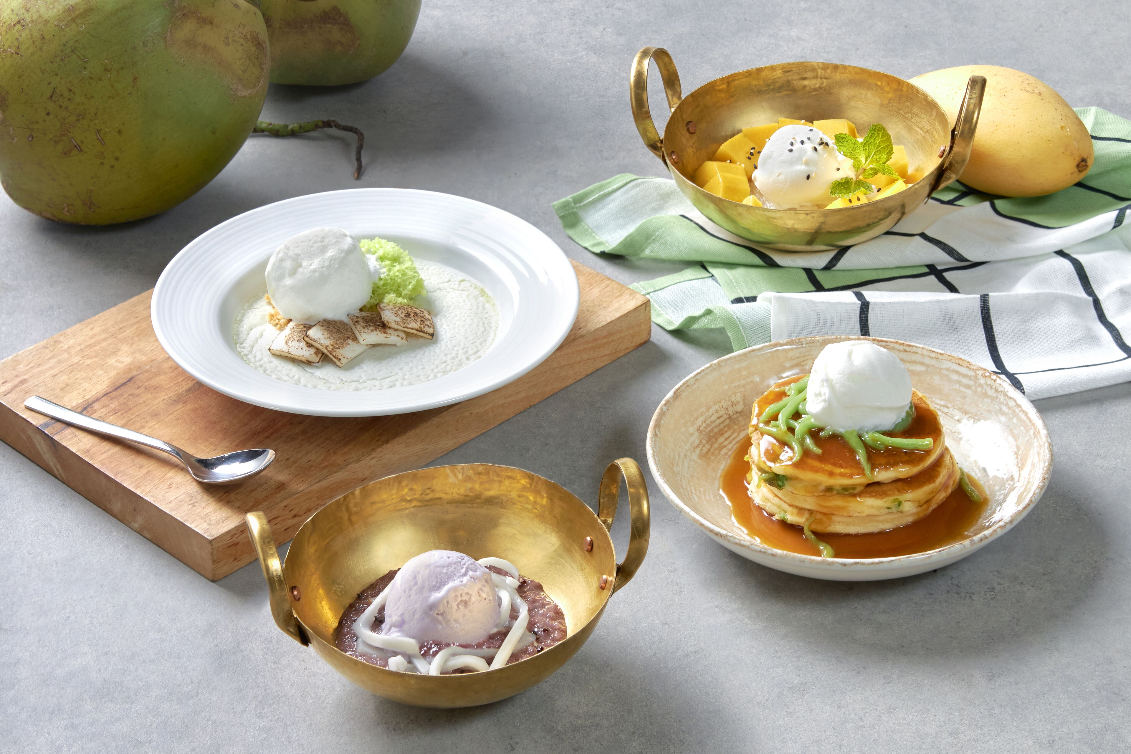 Een tafel met diverse gerechten, waaronder pannenkoeken, een kom mango en een bord met toetjes.