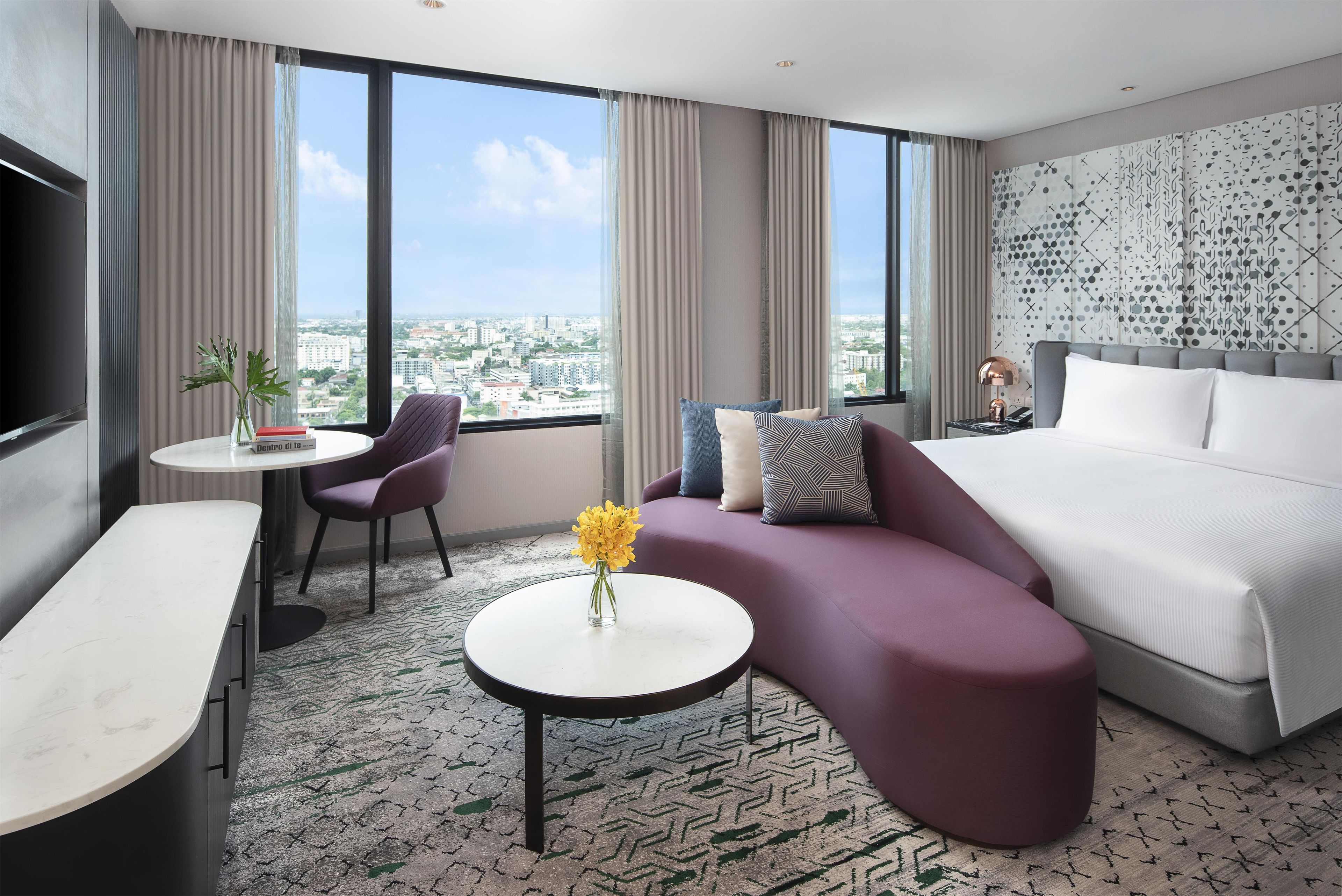 A modern hotel room with a bed, a sofa, a small table, and a TV.