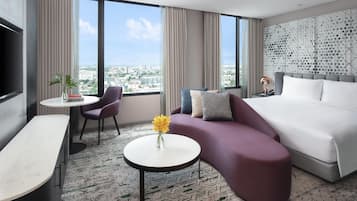 A modern hotel room with a bed, a sofa, a small table, and a TV.