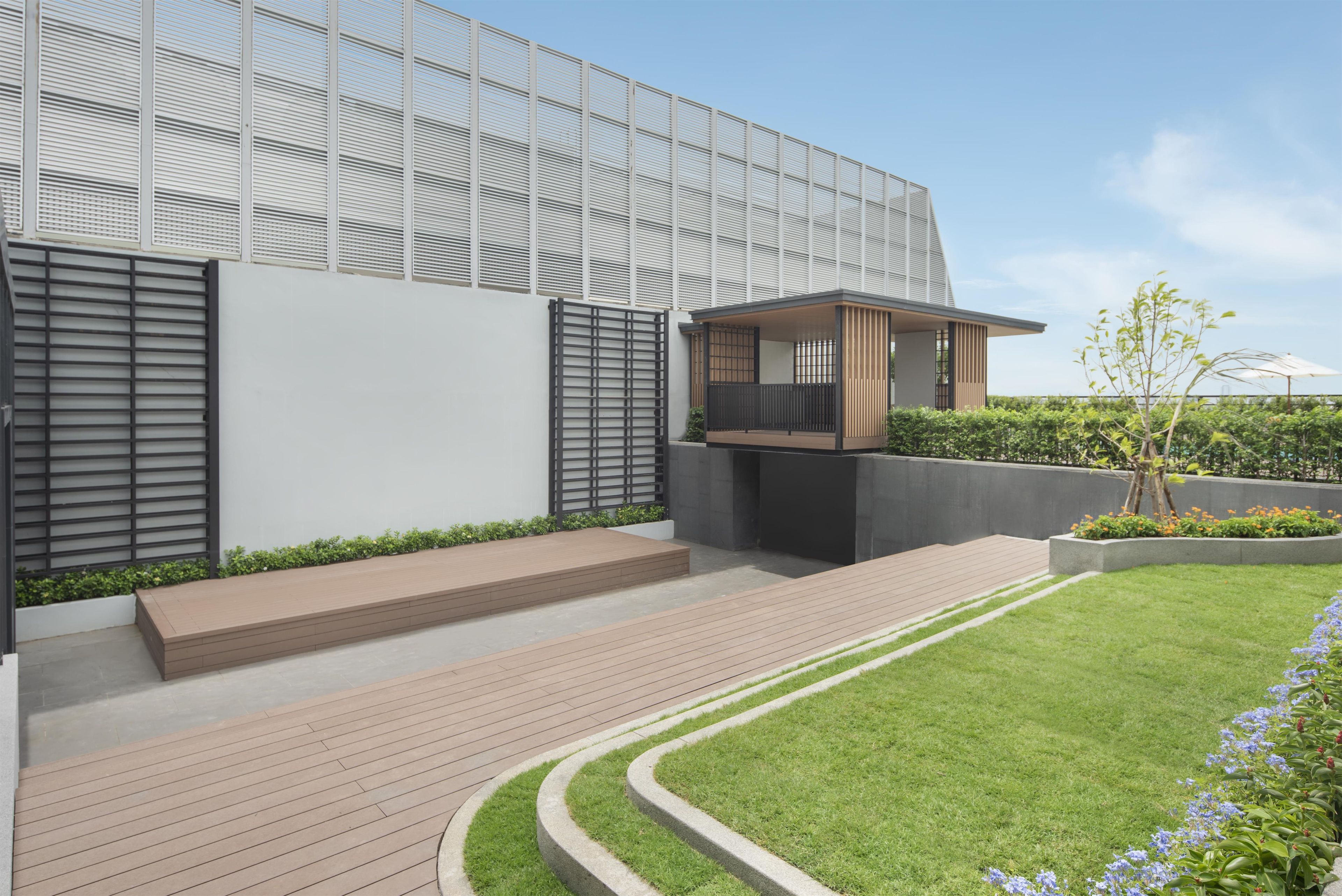 Un bâtiment moderne doté d’un toit plat, d’un espace extérieur couvert aménagé en coin salon et d’une pelouse bien entretenue.