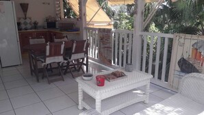 Eine überdachte Terrasse im Freien mit Esstisch, Stühlen und einer weißen Rattan-Couch.