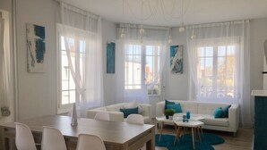 Una sala de estar moderna con comedor, que incluye una mesa de madera, sofás blancos y un tapete azul.