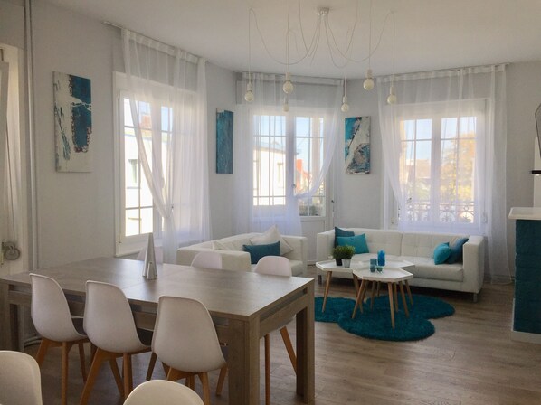 Ein modernes Wohnzimmer mit Essbereich, ausgestattet mit einem Holztisch, weißen Sofas und einem blauen Teppich.