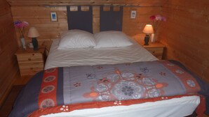 A wooden cabin bedroom with a bed, two bedside tables, a nightstand, a lamp, and a vase with flowers.