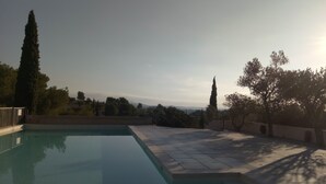 A swimming pool with a clear view of the surrounding landscape, including trees and distant mountains. - Mas Provençal first floor living room with fireplace and veranda overlooking Alpilles- Vallée des Baux (Paradou)