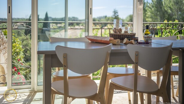 A balcony with a table and chairs, a wicker basket with bread, and a bottle of olive oil. - Mas Provençal first floor living room with fireplace and veranda overlooking Alpilles- Vallée des Baux (Paradou)