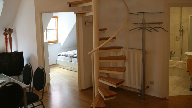 A modern interior with a spiral staircase, a dining area with chairs, a bed in the background, and a bathroom with a shower and sink. - Wendlers Ferienwohnungen 1 (Schwaig bei Nuernberg)
