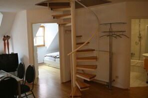Un intérieur moderne avec un escalier en colimaçon, un coin repas avec des chaises, un lit en arrière-plan et une salle de bain avec une douche et un lavabo.