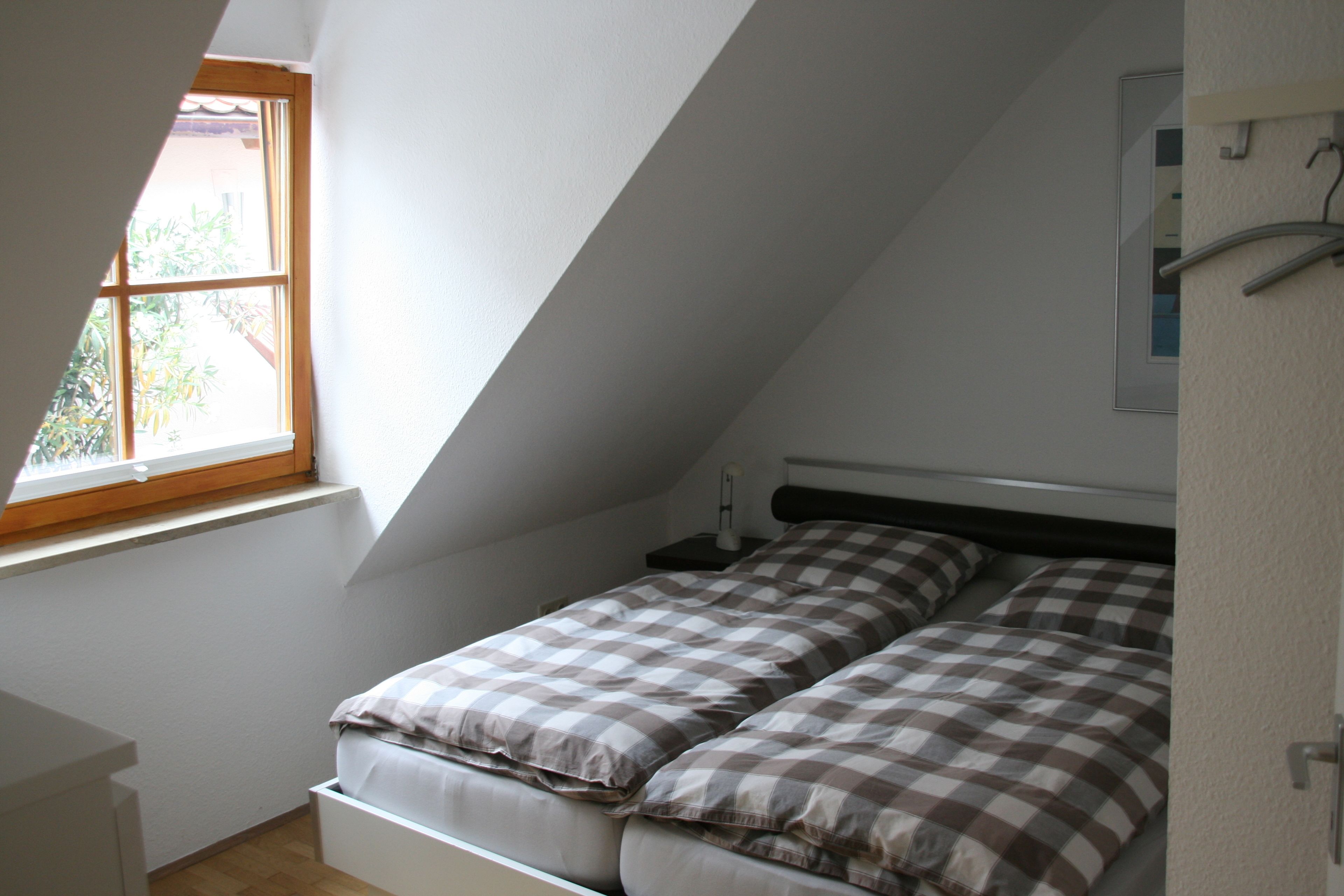 Ein kleines Zimmer mit einem Einzelbett, geneigter Decke und einem Fenster für natürliches Licht.