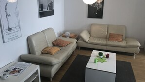 A modern living room with two beige sofas, a white coffee table, and a black rug. There are framed artworks on the wall and a white floor lamp. - Wendlers Ferienwohnungen 1 (Schwaig bei Nuernberg)