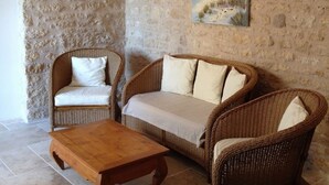 Une pièce avec un mur en pierre, des meubles en osier, une table en bois et un tableau sur le thème de la plage.