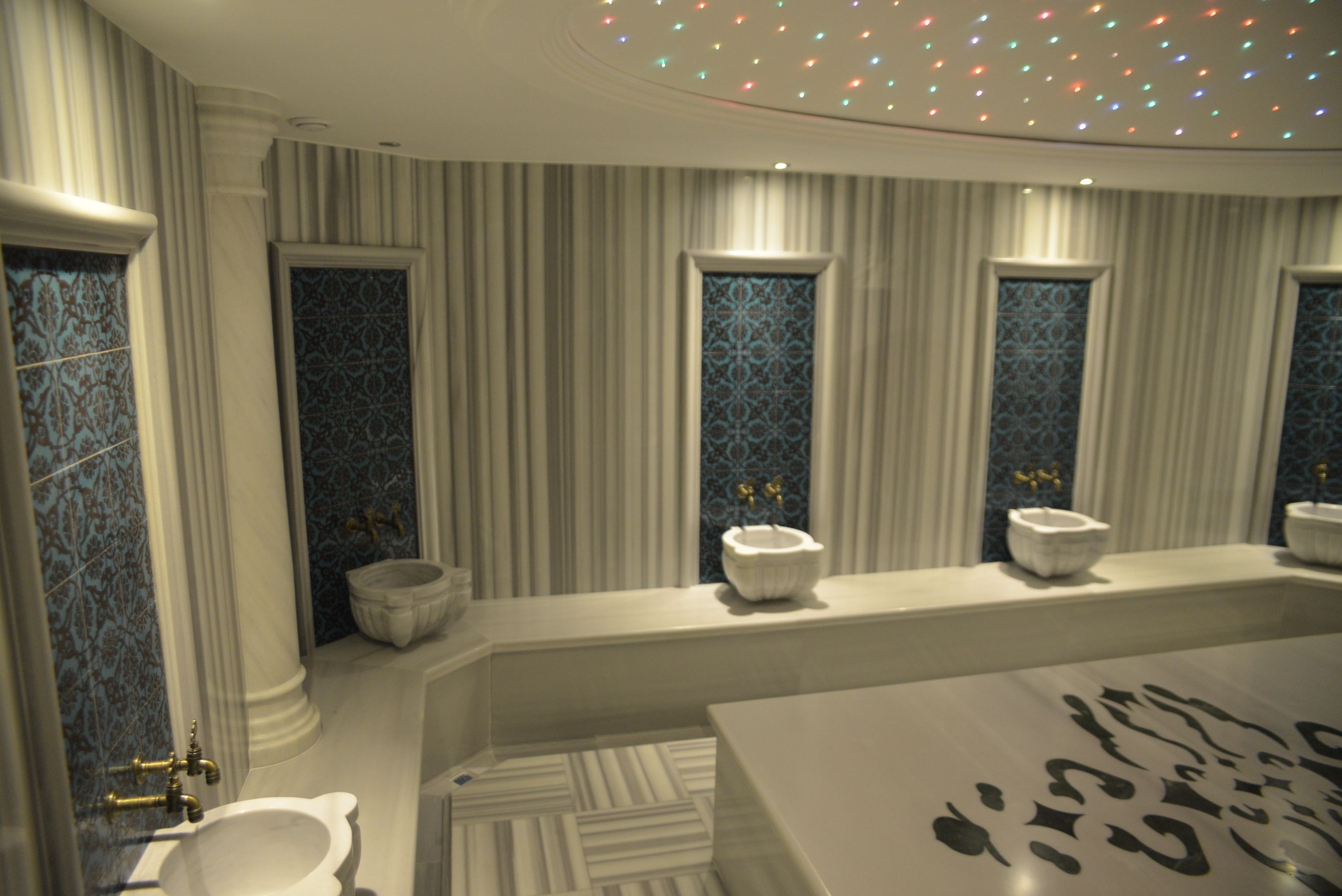 Un baño con una bañera grande, un inodoro y un bidé. Hay azulejos decorativos en las paredes y una alfombra estampada en el suelo.