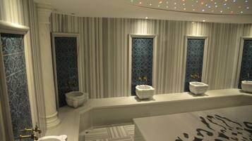Un baño con una bañera grande, un inodoro y un bidé. Hay azulejos decorativos en las paredes y una alfombra estampada en el suelo.