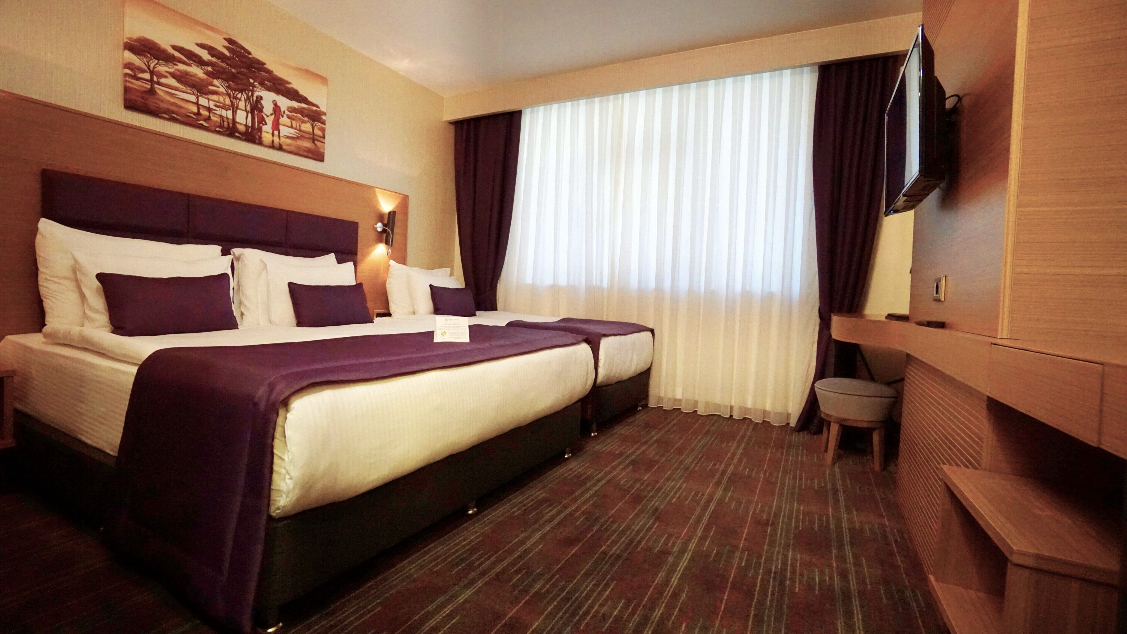 A hotel room with a large bed, a smaller bed, a desk, a chair, a television, and a painting on the wall.