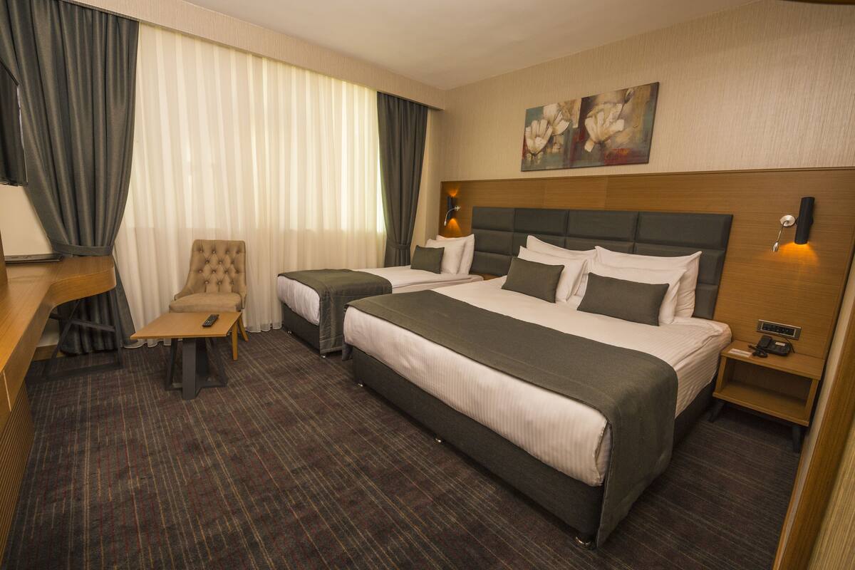 Een hotelkamer met twee bedden, een bureau, een stoel en een schilderij aan de muur.